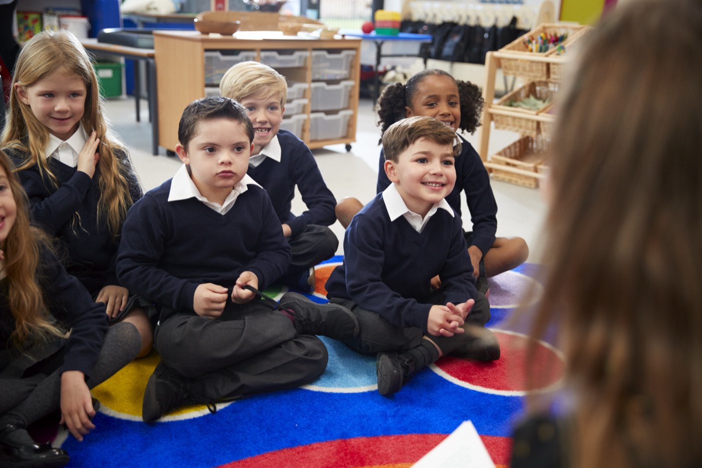 Children sitting together on a classroom carpet, listening to an adult